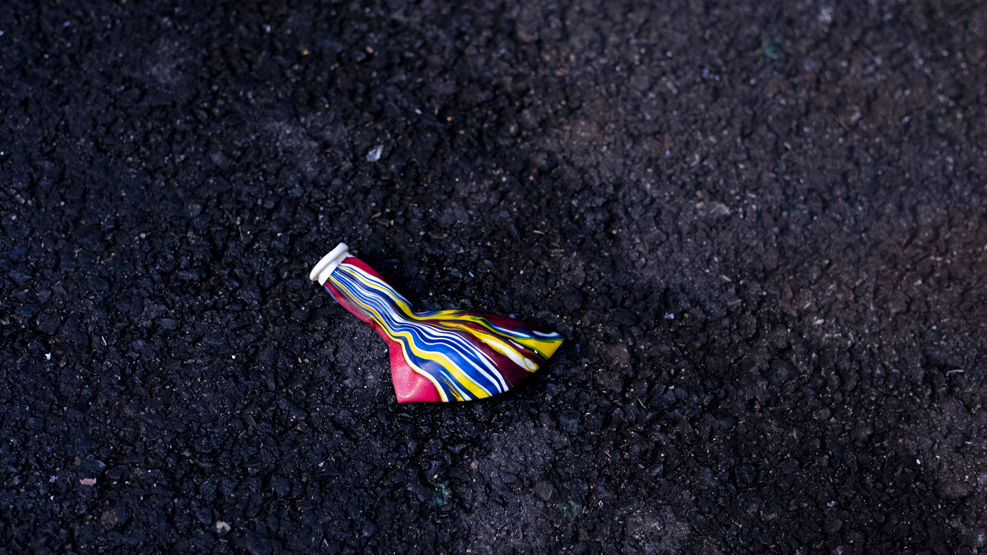 deflated rainbow balloon on black asphalt