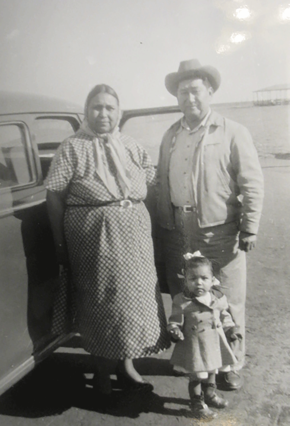 Black and white photo of an older couple with a young child, standing next to a car.